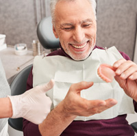 Man holding new dentures in dentist’s office 