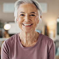 Older woman in purple shirt smiling with new dentures 
