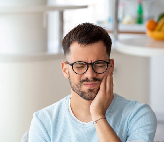 Man with glasses rubbing jaw in pain