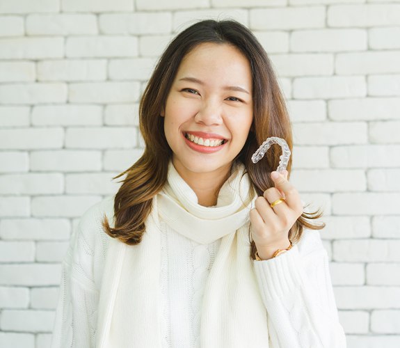 Woman in white sweater holding invisalign tray