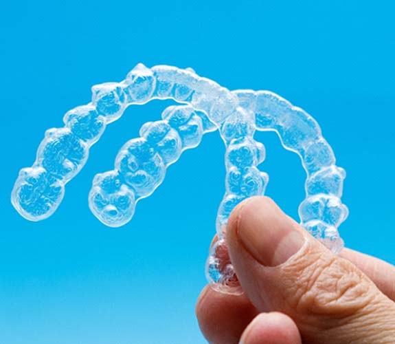 Hand holding two Invisalign aligners against blue background