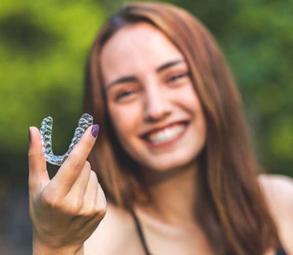 Woman with painted fingernails holding Invisalign aligner in foreground