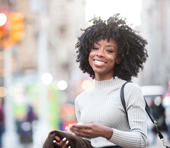 Woman in sweater outside smiling with tooth-colored fillings in Aurora, IL