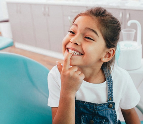 Girl smiling and pointing to teeth after Phase 1 orthodontics in Aurora, IL