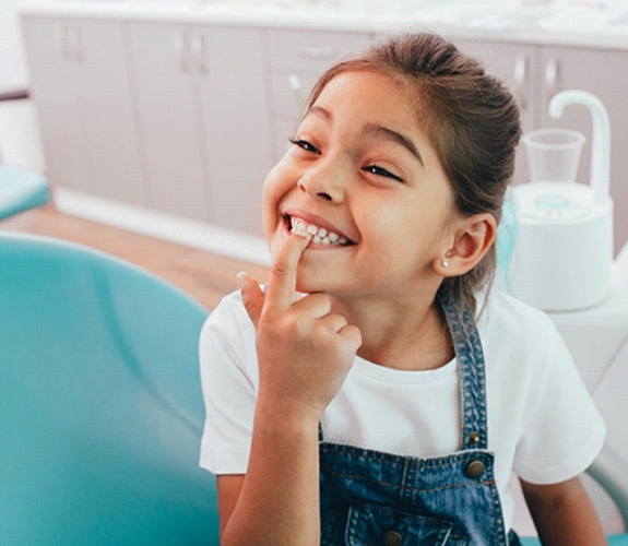 Little girl pointing to smile after restorative dentistry for kids in Aurora, IL