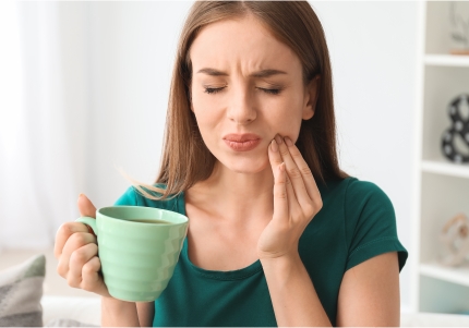 woman holding coffee cup and holding cheek in pain