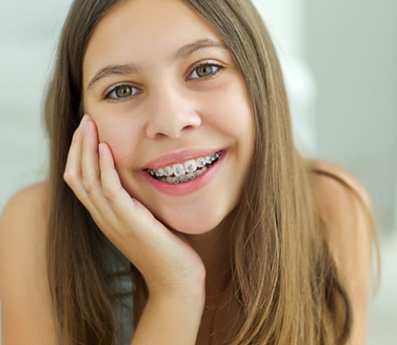 Young girl lying down and smiling with traditional metal braces in Aurora, IL