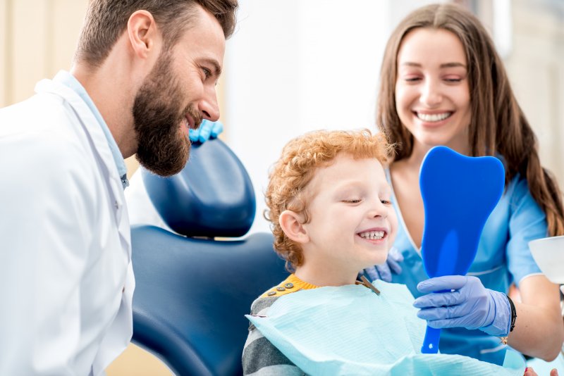 Son checking smile with mother and dentist watching