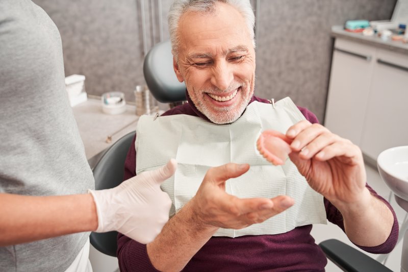 older man holding a denture at the dentist’s office