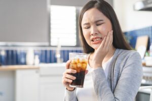 Woman holding her cheek in pain while also holding a beverage